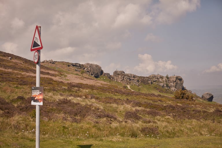 Cow and Calf rocks on the moor above Ilkley under a blue sky, beside a 17.5 per cent gradient road sign.