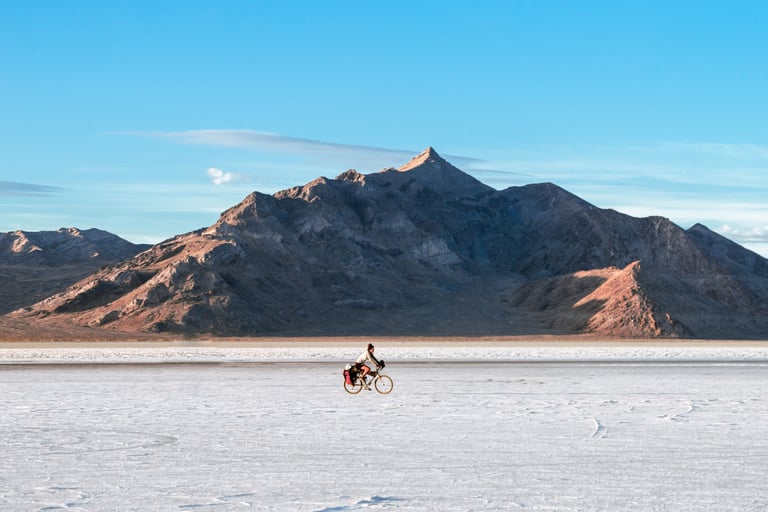 Rider crosses a white salt flat below a rocky mountain in the US, one of the Cycling Through A Pandemic stories.