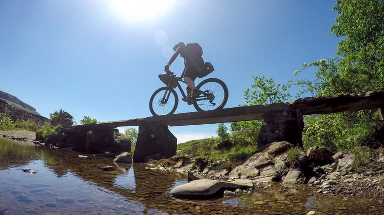 Rider crosses a stone slab bridge over a stream on a bikepacking route in the Yorkshire Dales.