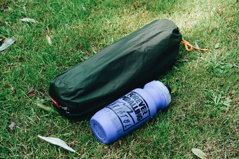 Fully packed Alpkit Elan hooped bivvy in its green drawstring bag, lying next to a 500ml bottle.