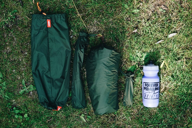 Alpkit Elan hooped bivvy packed into green stuff sacks laid out on grass beside a 500ml bottle for scale.