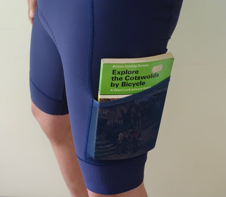 Victory Chimp Out There cargo bib shorts with a pocket holding a vintage Explore the Cotswolds by Bicycle guidebook.