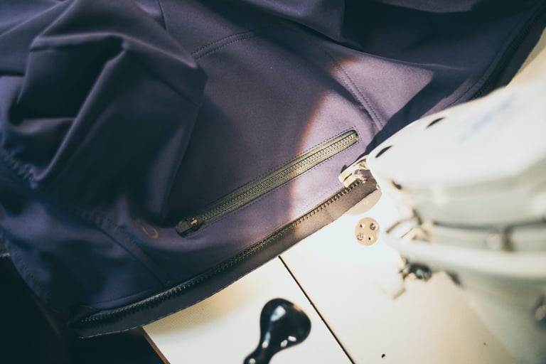 Zip repair on a navy cycling garment next to a sewing machine, part of the Velocio and Apidura repair scheme.