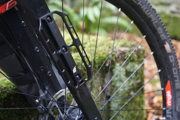 Small Tailfin Cargo Cage bolted to a black fork beside a Schwalbe G-One tyre, with a fork bag just visible behind.