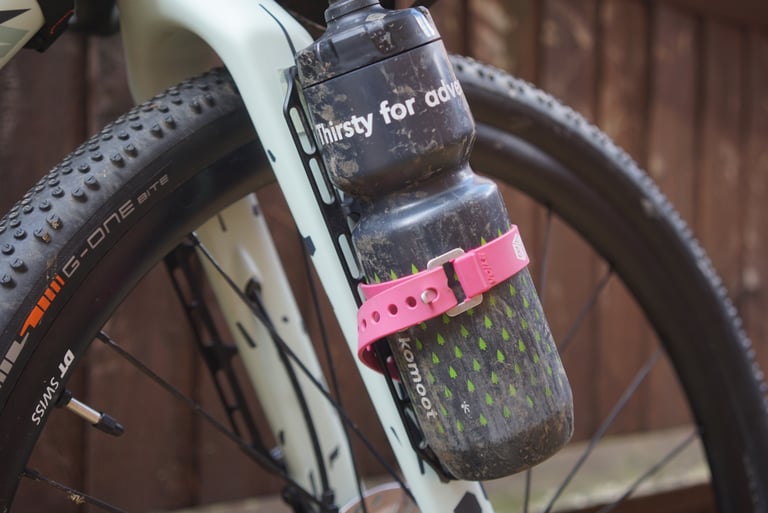 Tailfin Cargo Cage with Load Chip on a gravel bike fork holding a muddy bottle secured by a pink Voile strap.