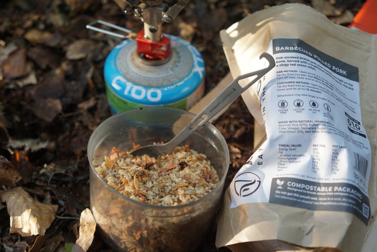 Dried Firepot BBQ pulled pork and rice in a cup beside its compostable pack, a gas canister and stove.