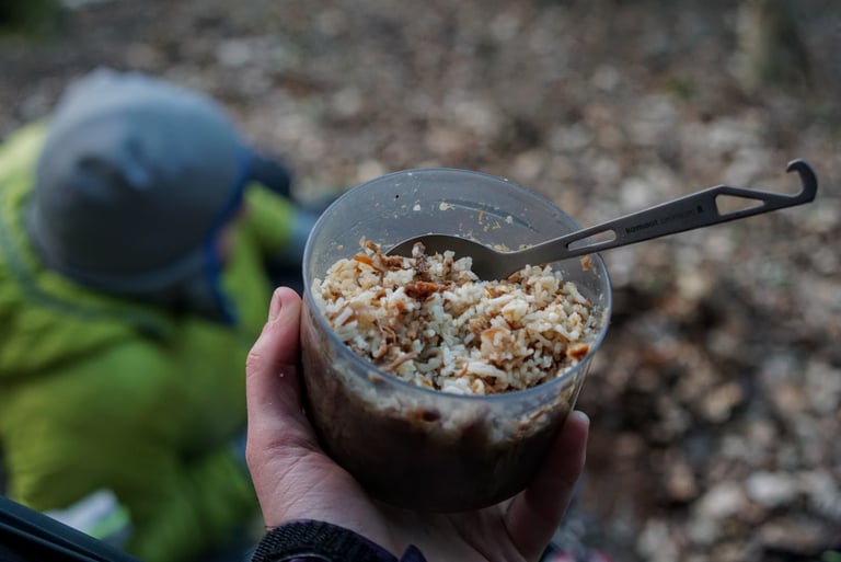 Firepot BBQ Pulled Pork rehydrated with rice in a cup, held up on a bikepacking trip in woodland.