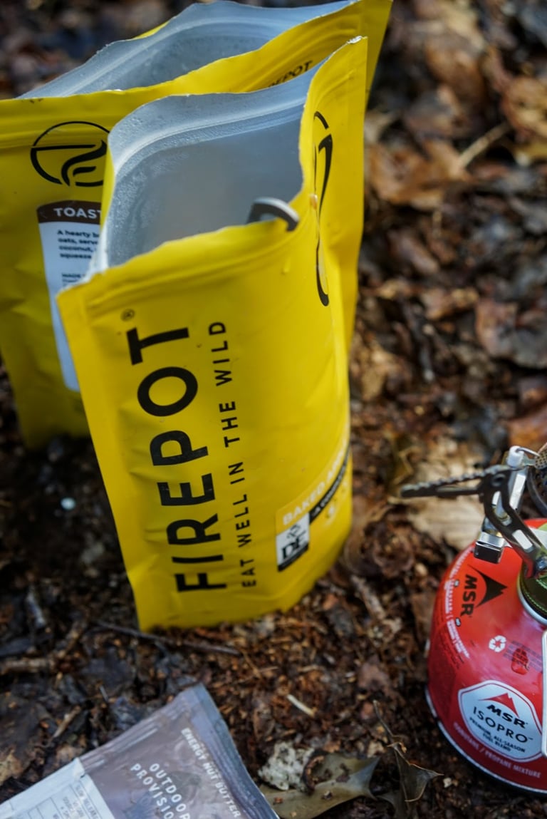 Open yellow Firepot Food packet standing upright beside an MSR gas canister and an Outdoor Provisions sachet.