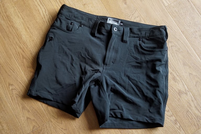 Chrome Industries Anza women's shorts in black laid flat on a wooden floor, showing the nylon-spandex fabric.