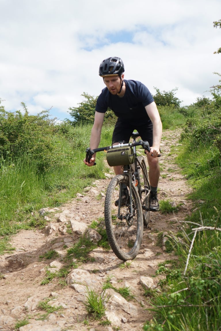 Rider descends a rocky East Devon bridleway on a gravel bike with 52cm Cowchipper Deluxe bars and a bar bag.