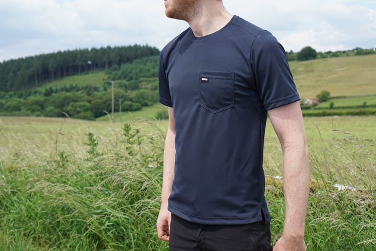 Chapeau Dry Tech Tee in Deep Ocean navy, with a chest pocket, worn in a grassy field below a wooded hill.