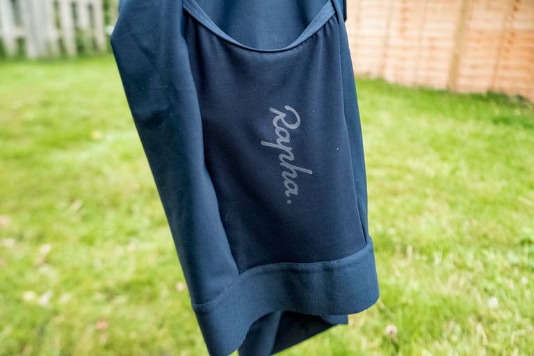 Navy Rapha Core Cargo shorts hanging outdoors, showing the logo on the mesh cargo pocket and the leg hem.