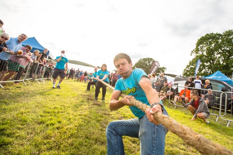 Gritfest tug of war, a man in a blue top leaning back on the rope as spectators watch from behind barriers.