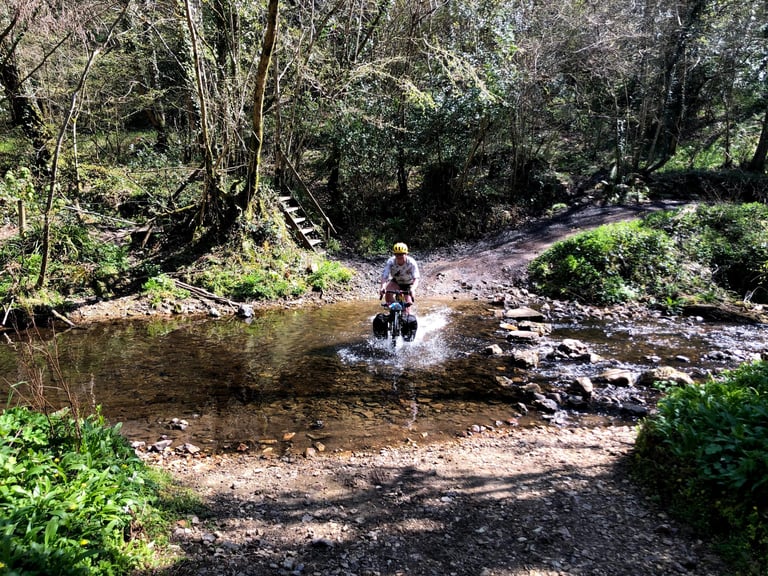 Rider splashes through a shallow ford on a loaded bike with Restrap panniers, testing their waterproofing.