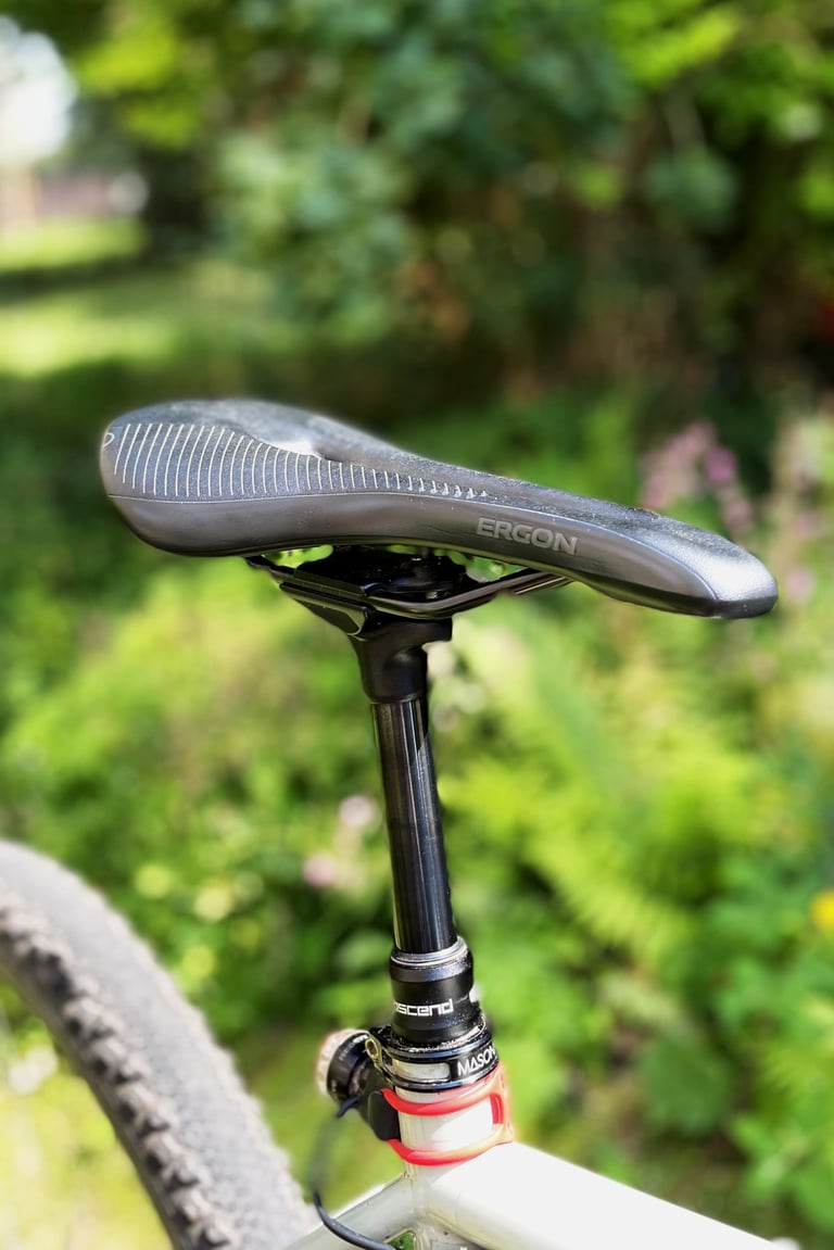 Side view of an Ergon SR Pro saddle on a dropper seatpost, with a knobbly tyre below.