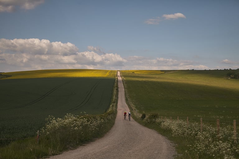 Two riders on the Wessex Ridgeway climb a long gravel track between fields on the Leeds to Lyme Regis route.