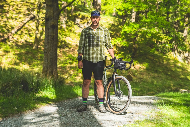 Rider in Lusso Adventure bib shorts stands with a gravel bike on a forest track, showing the fit.