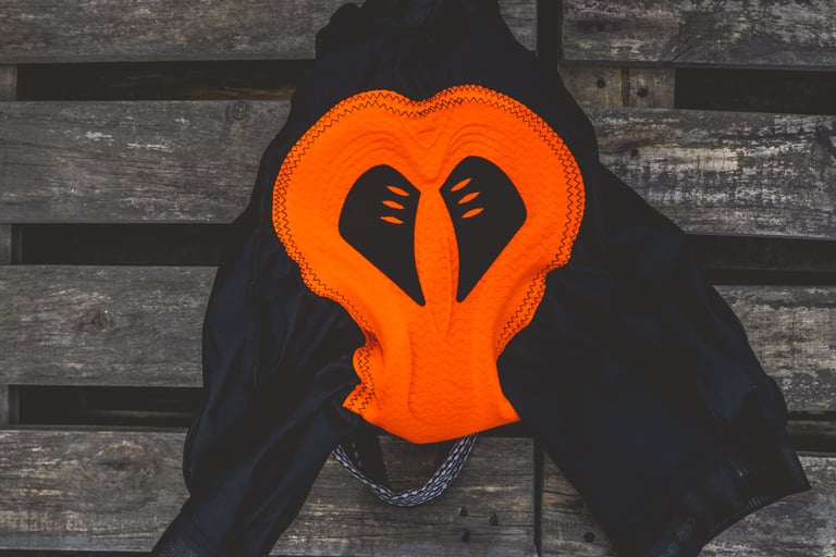 Inside of the Lusso Adventure bibs on wooden boards, showing the orange endurance chamois pad.