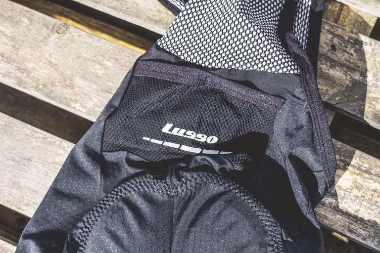 Lusso logo and reflective stripe on the rear pocket of the Adventure bib shorts, laid on wooden slats.