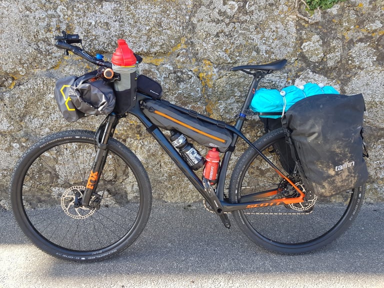 Gail Brown's Scott hardtail with Fox fork, bar bag, frame bag and Tailfin pannier leans against a stone wall.