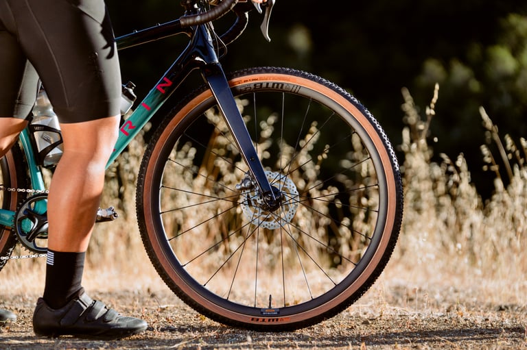 Front WTB CZR i23 carbon wheel with tan-wall tyre on a teal gravel bike, seen from the side beside a rider's legs.