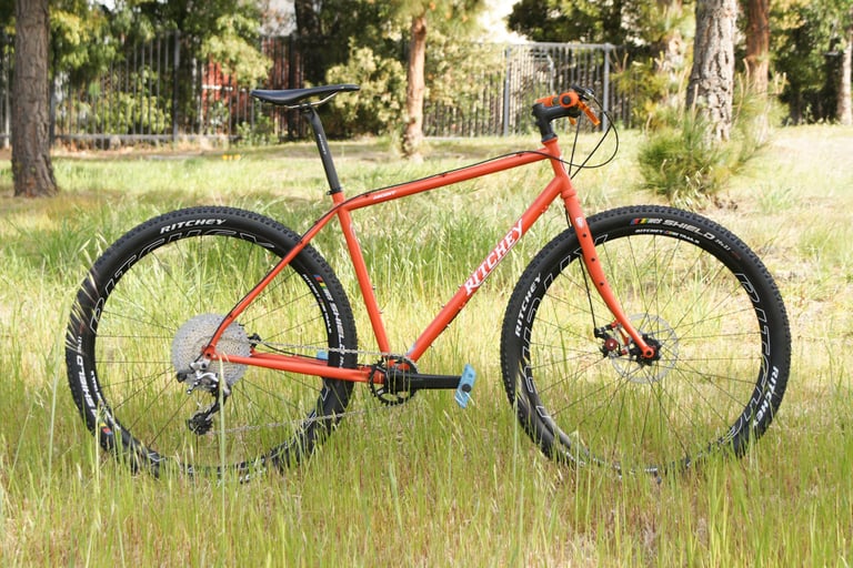 Complete 2021 Ritchey Ascent in Sierra Red with flat bars and Ritchey tyres, side view in long grass.