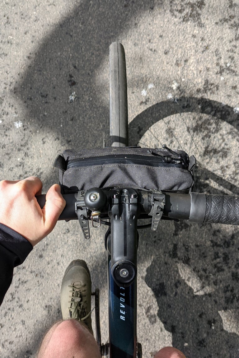 Looking down at the Giant Revolt Advanced Pro 0 cockpit, with a hand on the bar and a small bag on the front.