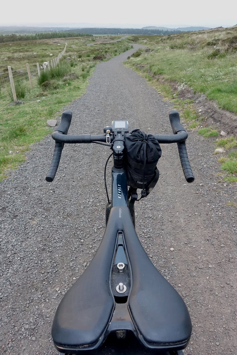 View over the saddle and handlebar of the Giant Revolt Advanced Pro 0 on a gravel track across moorland.