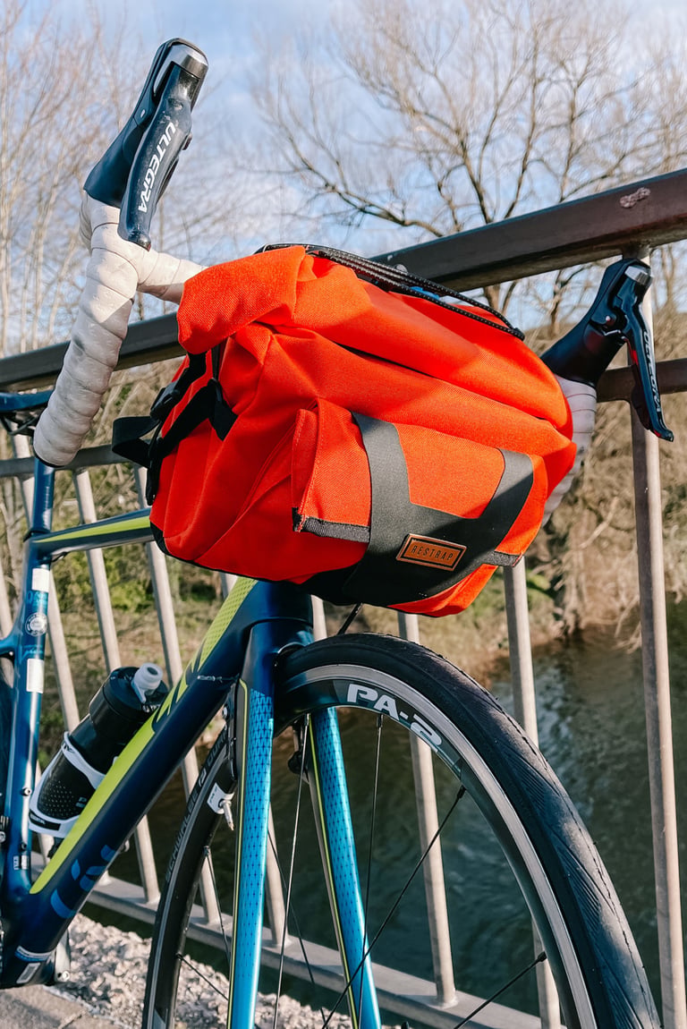 Orange Restrap Bar Pack fitted to the drop handlebars of a road bike, with a river behind.
