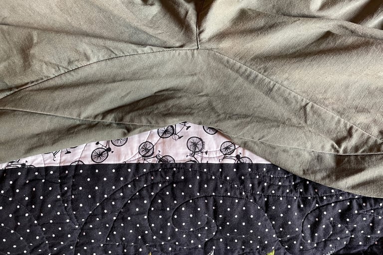 Close-up of the diamond gusset seam on moss-coloured Vulpine men's gravel shorts laid on a bicycle-print quilt.