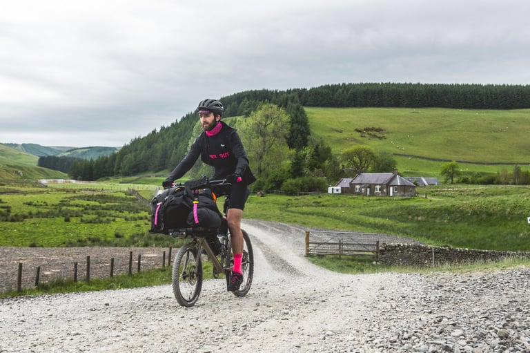 Farr Out Deliveries rider on the loaded Rothair mini cargo bike rides a gravel track past a cottage and forestry plantations.