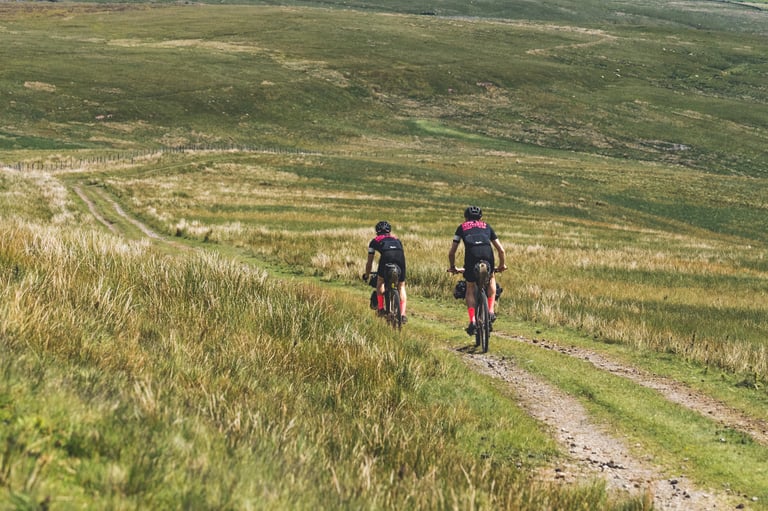 Two Farr Out Deliveries riders follow a grassy double track across open moorland on the Pennine Rally.