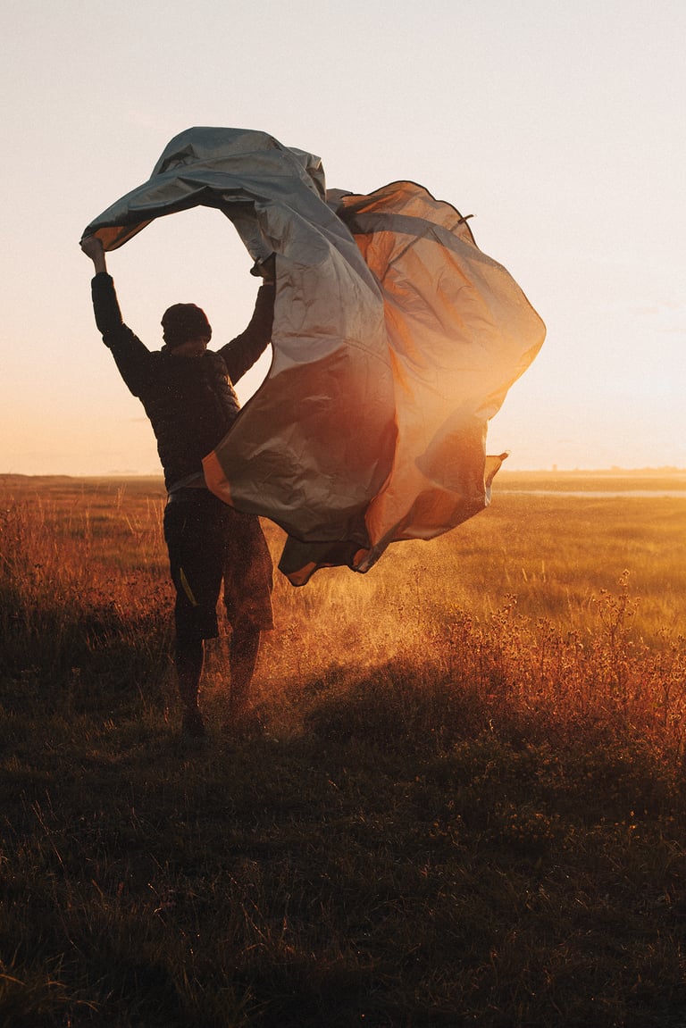 Camper shakes out a tarp against the golden sunrise while packing up after the overnight bivy.
