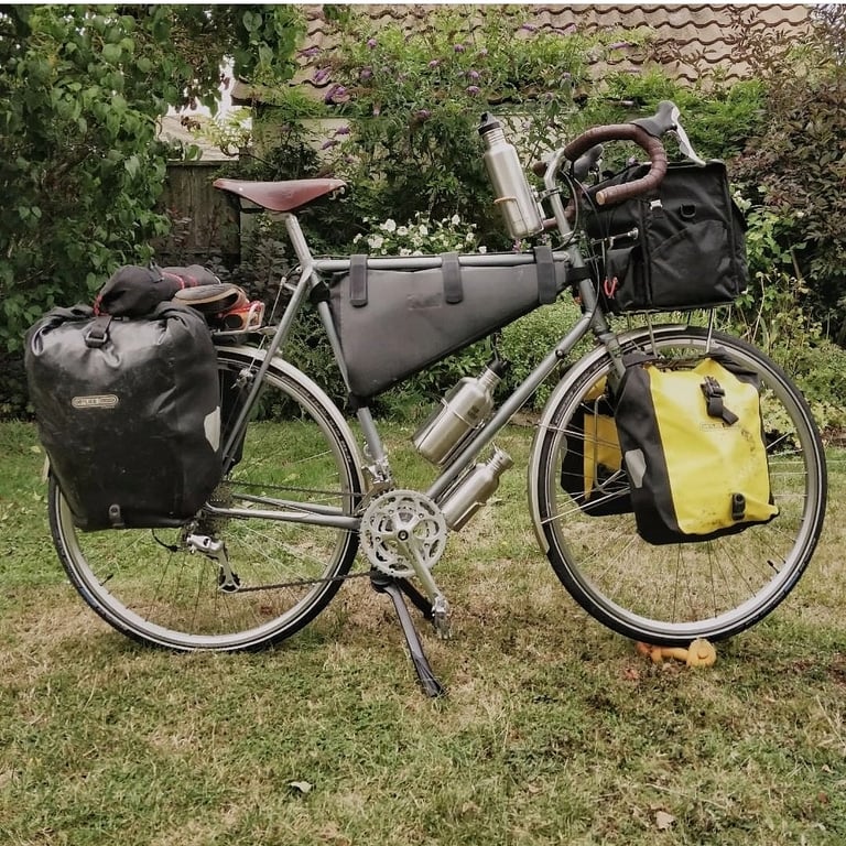Fully loaded touring bike with Ortlieb panniers, a frame bag and a bar bag, standing on a garden lawn.