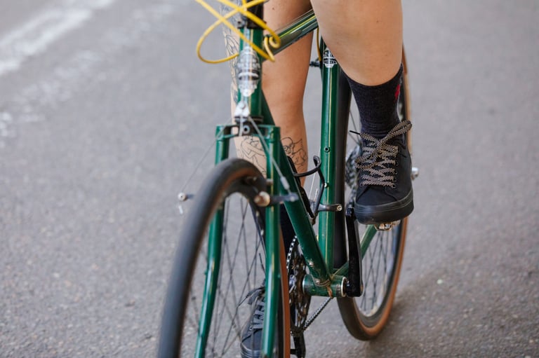 Rider on a green bike pedals along a road in black Chrome Panaracer Pedal Series trainers with reflective laces.