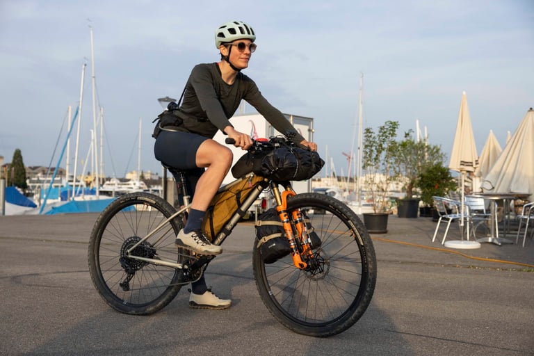 Quinda Verheul rides a bikepacking mountain bike with frame and bar bags along a harbour front.