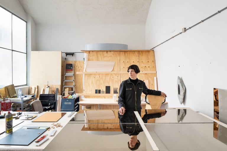 Quinda Verheul stands in her Rotterdam studio behind a mirrored table, with a stone sculpture on the wall.