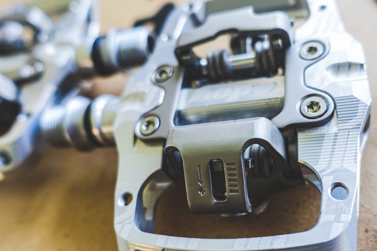 Hope Union Trail pedal's cleat clip with its plus and minus tension markings, the second pedal blurred behind.