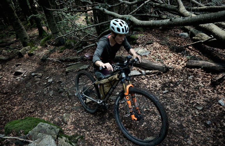 Quinda Verheul pushes a loaded mountain bike up a rocky forest trail strewn with fallen branches.