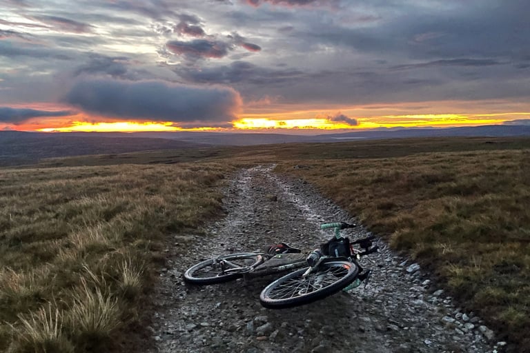 Loaded bike lies on a stony track on Cross Fell as orange sunrise colours the sky over the Pennines.