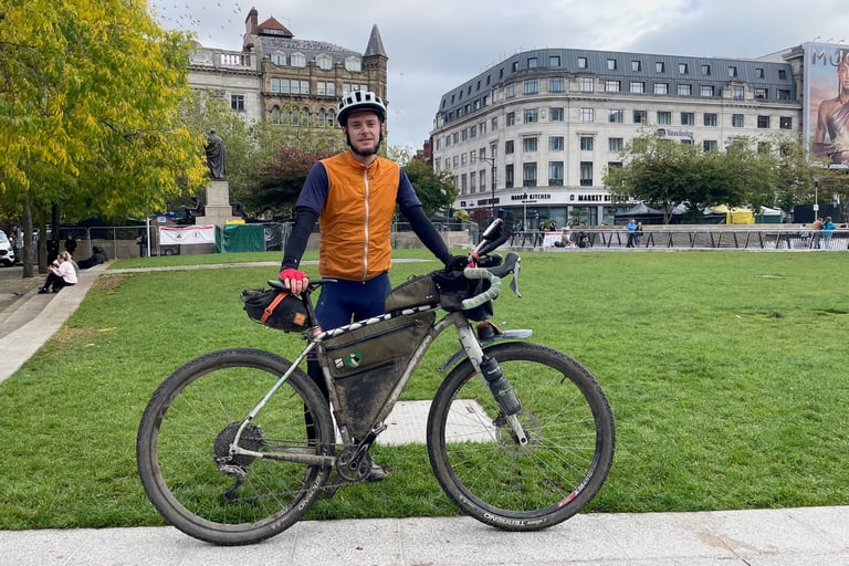 Marcus Nicolson stands with his muddy loaded bike on a lawn in Manchester city centre at the end of the Second City Divide.