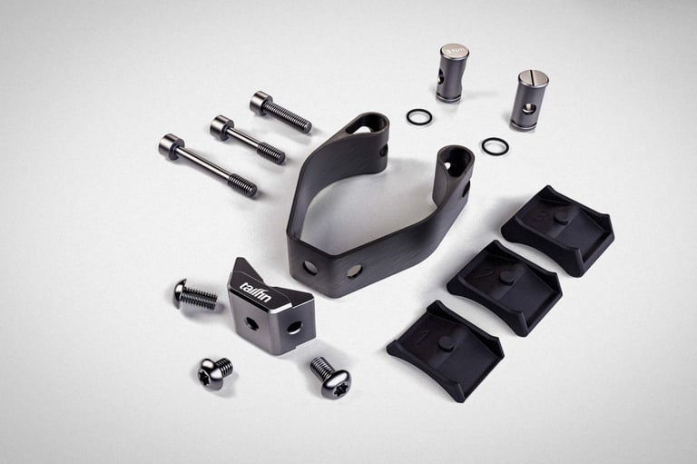 Tailfin Suspension Fork Mount carbon clamp with barrel nuts, bolts, O-rings and numbered shims laid out on white.