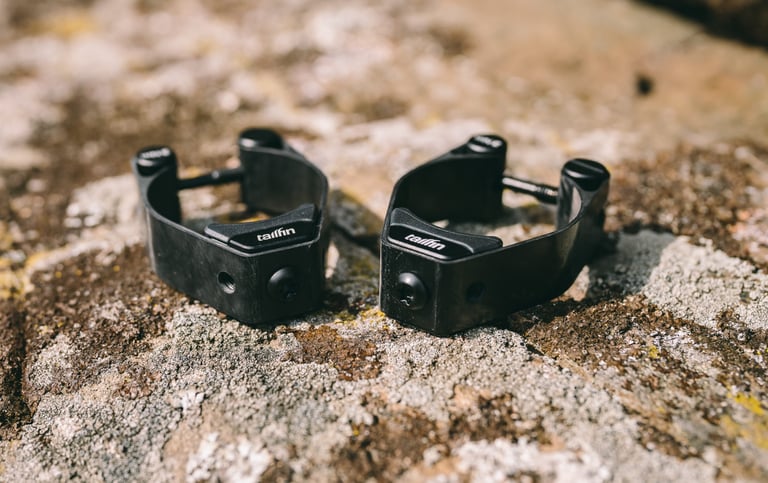Pair of black Tailfin Suspension Fork Mount clamps resting on a lichen-covered rock.