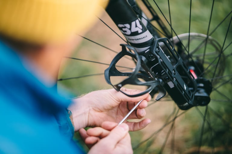 Rider fitting a bottle cage to a Tailfin Suspension Fork Mount on a fork leg using a hex key.