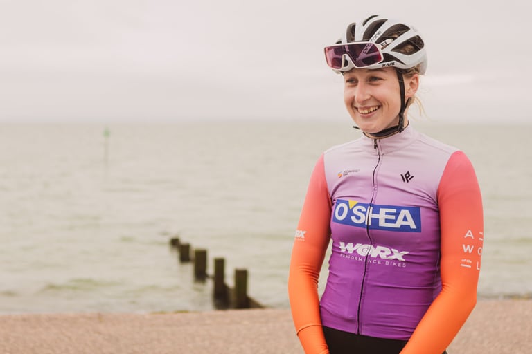 Phoebe Martin of AWOL O'Shea smiles in team kit beside the Thames Estuary after stage 4 of the Women's Tour of Britain.