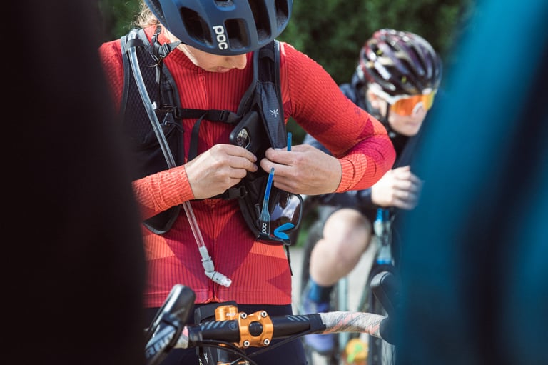 Rider in a red jersey tucks a phone into the zipped chest pocket of the Apidura Racing Hydration Vest.