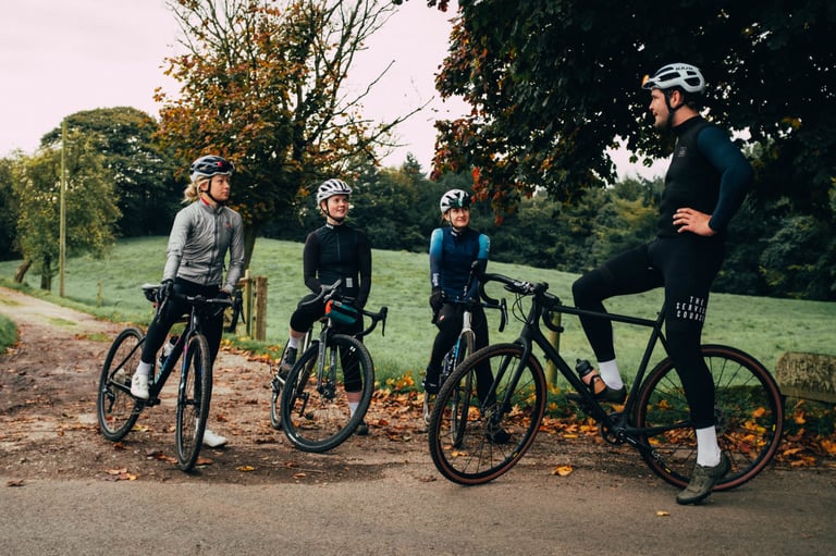 Four riders on gravel bikes chat under autumn trees at a lane junction during the Service Course Gravel Bonanza.
