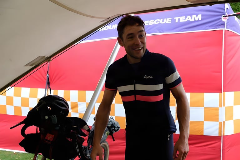Chris Hinds smiles under a red Mountain Rescue Team gazebo, loaded bike beside him, after the Great British Divide.