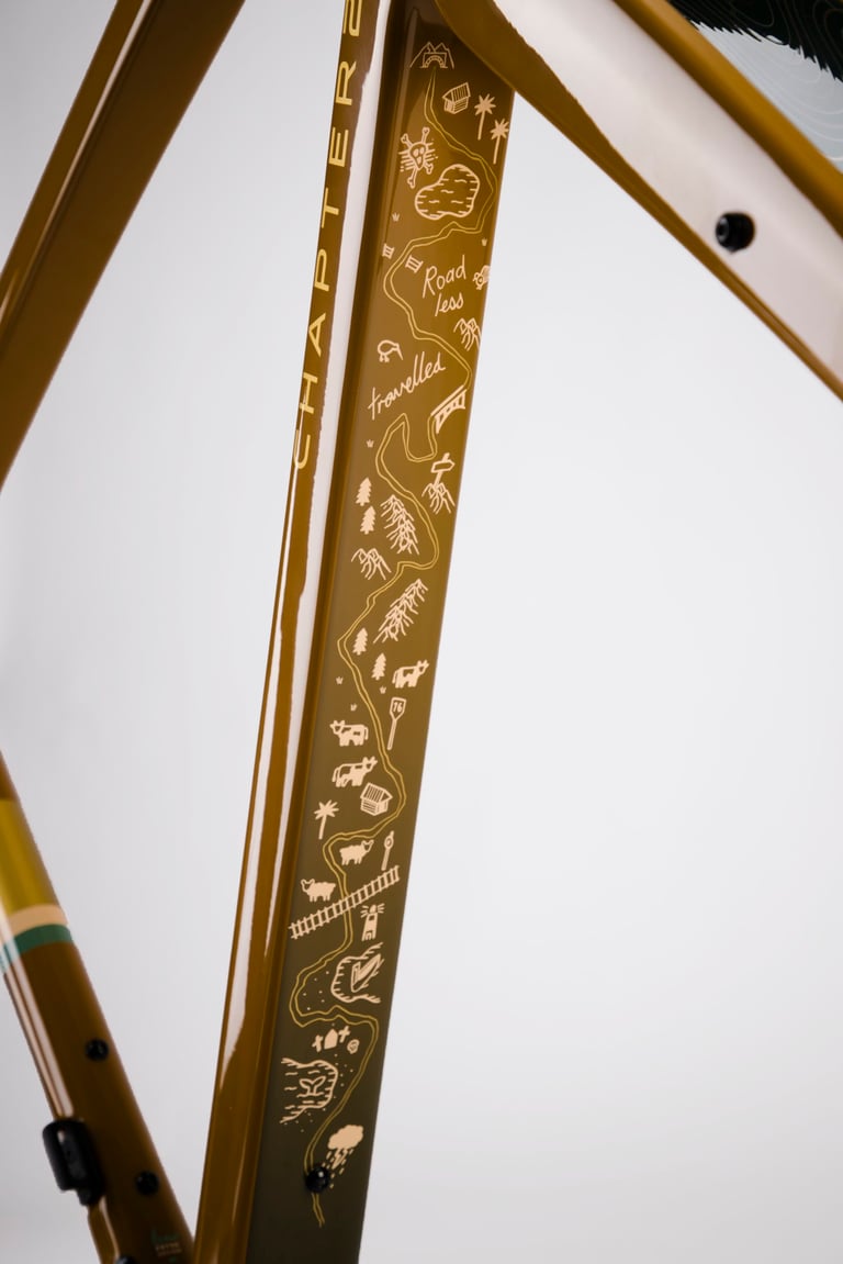 Hand-drawn map graphic reading "Road less travelled" along a bronze tube of the Chapter2 AO Rangipo frame.