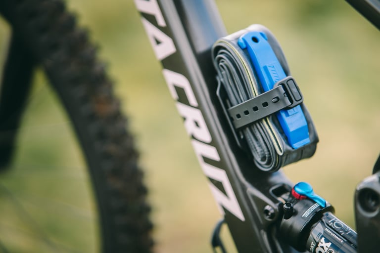 Spare inner tube and blue tyre lever strapped to a Tailfin Mini Cage on a mountain bike frame.